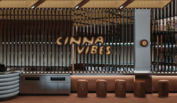 Cinnavibes Interior of a modern café with brown stools, metallic accents, and a sign reading “Cinna Vibes” on a wall with vertical wooden slats, creating the perfect atmosphere for enjoying signature cinnamon rolls at Cinnavibes. Cinnamon Rolls